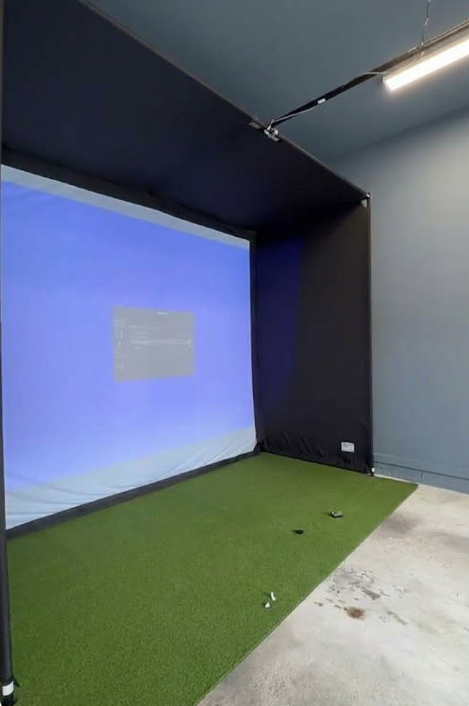 PlayBetter SimStudio golf simulator enclosure in a garage with the screen lit